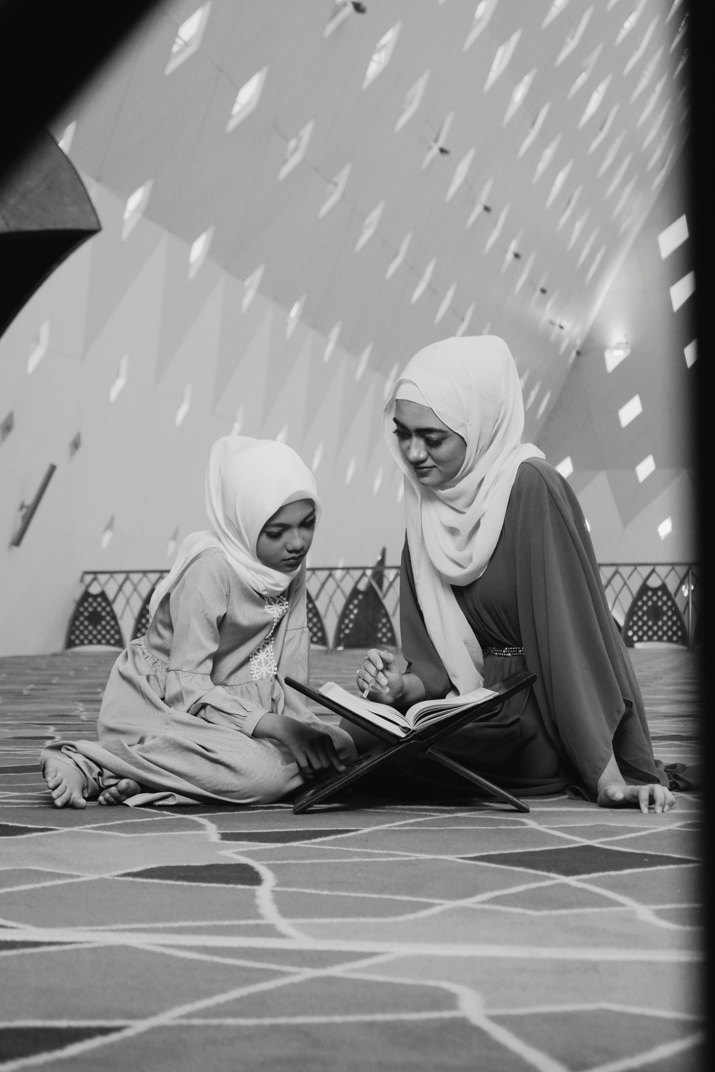 A mother helping her daughter read the Qur’an in a mosque